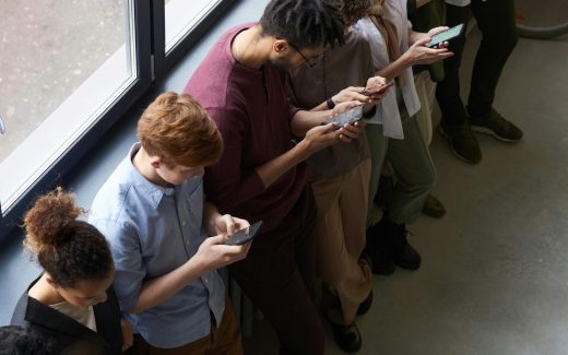 A group of diverse office workers standing by a window using smartphones, capturing modern workplace connectivity.